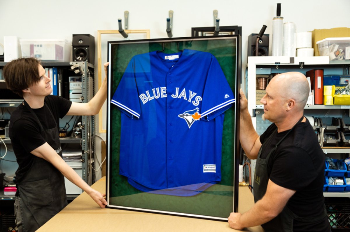 2 men displaying a framed jersey